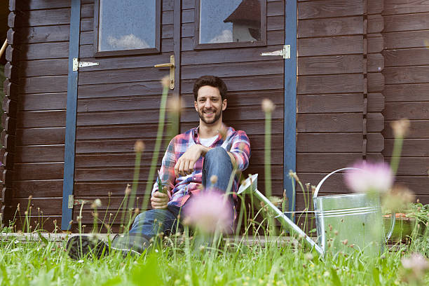 Homme souriant appuyé contre un abri de jardin en bois